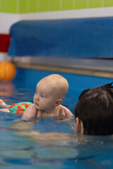 Portrait of the curious baby looking around in a swimming pool. Closeup. Swimming with a coach.