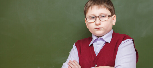 boy standing with his arms crossed at a school board. in glasses and school uniform