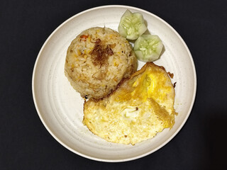 Fried rice served with sunny side up egg and fresh cucumber slices on a white plate, looks very delicious.