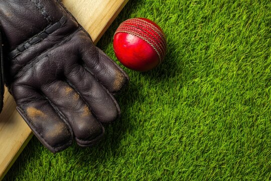Leather cricket glove and red seam ball with wooden bat on lush grass pitch, premium cricket equipment optimizing match performance.