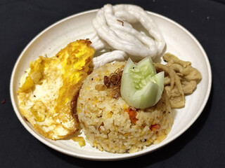 Fried rice served with sunny side up egg and fresh cucumber slices on a white plate, looks very delicious.