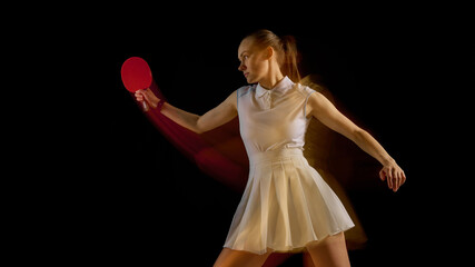 Table tennis player swinging paddle with motion blur in athletic pose on dark background. Concept...