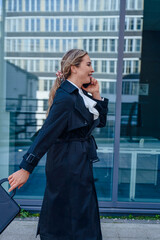 Young professional walking confidently in a city while talking on the phone, wearing a stylish coat...