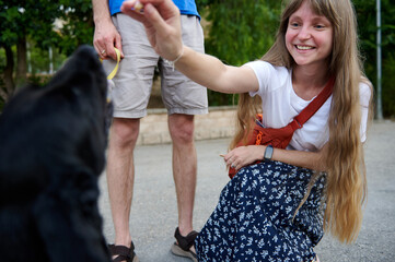 Young Woman Smiling While Giving Treats to a Black Dog Outdoors