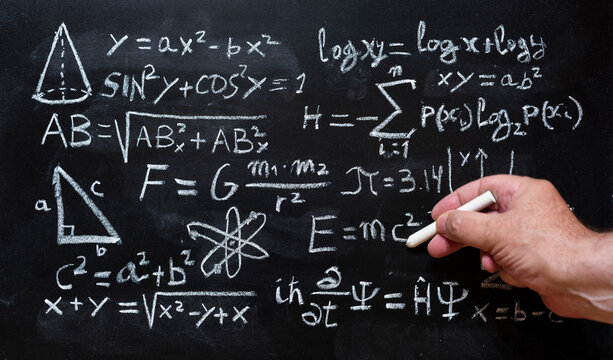 Mano escribiendo operaciones y formulas de física cuántica y matemáticas con una tiza en la pizarra
