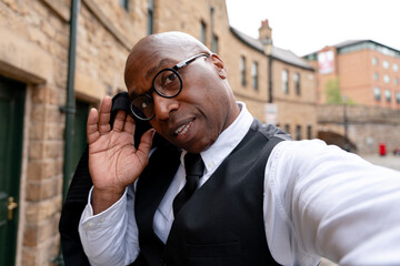 Portrait of a man in a vest and glasses posing in an urban setting with historical buildings and...