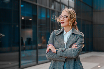 Businesswoman with glasses stands confidently outside a modern office building on a sunny day,...