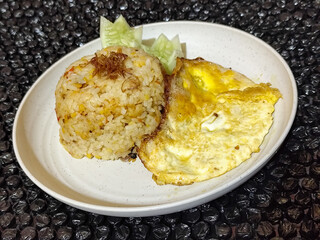 Fried rice served with sunny side up egg and fresh cucumber slices on a white plate, looks very delicious.