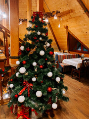 Festive Christmas tree decorated with red and white ornaments in cozy wooden cabin restaurant
