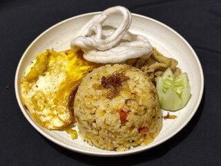 Fried rice served with sunny side up egg and fresh cucumber slices on a white plate, looks very delicious.