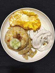 Fried rice served with sunny side up egg and fresh cucumber slices on a white plate, looks very delicious.