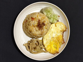 Fried rice served with sunny side up egg and fresh cucumber slices on a white plate, looks very delicious.