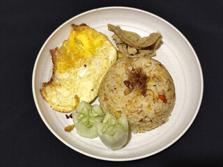 Fried rice served with sunny side up egg and fresh cucumber slices on a white plate, looks very delicious.