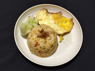 Fried rice served with sunny side up egg and fresh cucumber slices on a white plate, looks very delicious.