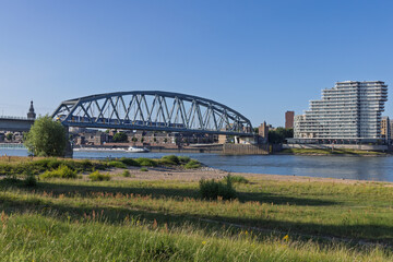 A view of the Spoorbrug bridge over the Waal River in Nijmegen, Netherlands, with a modern apartment building and green shore.