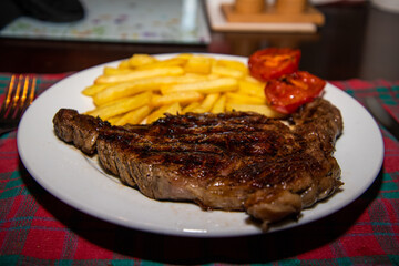 Deliciously cooked ribeye steak served with golden chips and grilled tomatoes on the side—a classic and hearty meal, perfect for steak lovers.