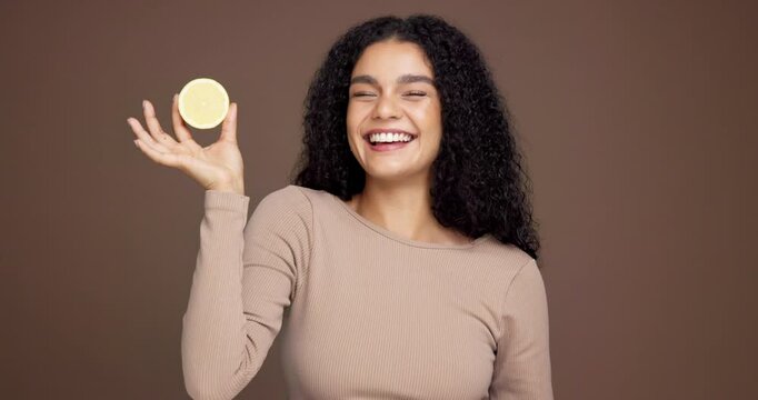 Happy woman, face and vitamin c with lemon in studio for citrus acid or detox on a brown background. Portrait, female person or model with smile or natural organic fruit for health or diet on space
