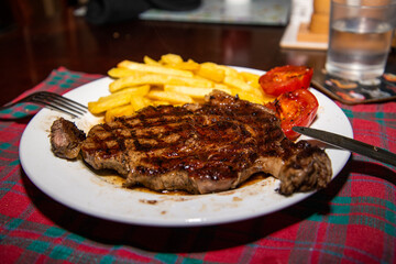 Deliciously cooked ribeye steak served with golden chips and grilled tomatoes on the side—a classic and hearty meal, perfect for steak lovers.