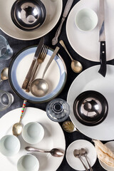 Top view of an empty plates, bowls, glasses and cutlery placed on a black chalkboard background....