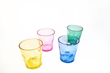 Four transparent plastic cups in yellow, pink, blue, and green arranged on a white background. Colourful drinkware with a modern, minimal look.