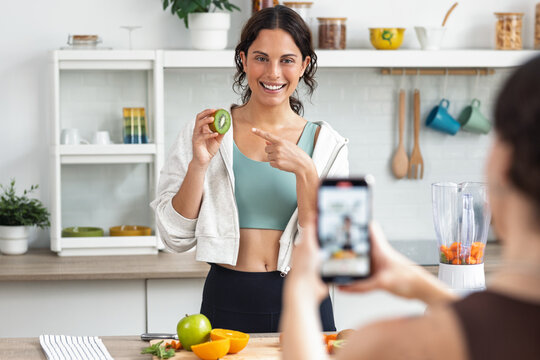 Influencer woman making a vegetable and fruit juice while being recorded with a smartphone in the kitchen
