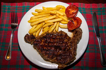 Deliciously cooked ribeye steak served with golden chips and grilled tomatoes on the side—a...