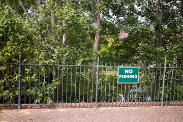 Green "No Fishing" sign mounted on metal railings at Enfield Island Village, with leafy greenery and the River Lea visible in the background—highlighting local regulations by the water.