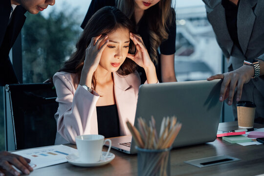 Stressed Asian businesswoman with colleagues looking at laptop in tense situation. Concept of deadline pressure, business crisis, teamwork, and urgent problem solving.