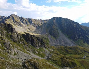 Fototapeta premium A mountainous landscape featuring rocky peaks and green slopes under a partly cloudy blue sky view from above