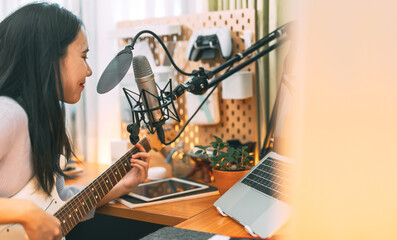 Asian woman singer on microphone playing electric guitar using technology live streaming at home studio