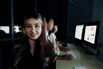 Smiling Asian businesswoman touches transparent virtual screen with stock graphs in background. Team analyzing financial data in modern office. Fintech and data interaction concept.