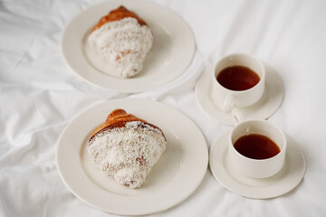 Two cups of coffee and croissants on a white sheet in the bedroom.