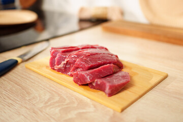 Freshly sliced raw beef laid on a wooden cutting board ready for cooking or preparation in a kitchen setting