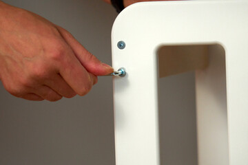 Person assembling a white furniture piece using a wrench in a well-lit indoor