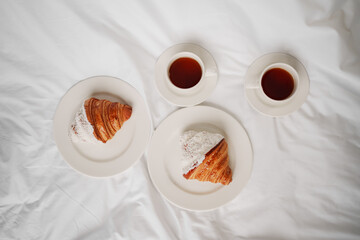 Two cups of coffee and croissants on a white sheet in the bedroom.