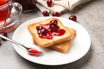 Toasts with tasty cherry jam, tea and fresh fruits on grey table , closeup