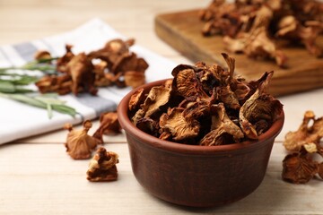 Dried chanterelle mushrooms in bowl on light wooden table, closeup