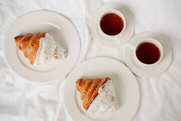 Two cups of coffee and croissants on a white sheet in the bedroom.