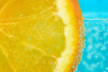 Bubbly orange slice submerged in sparkling water under bright blue background
