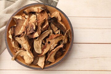 Pieces of dried mushrooms in bowl on light wooden table, top view. Space for text