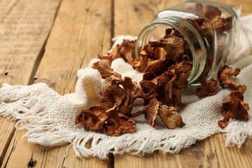 Dried chanterelle mushrooms in jar and towel on wooden table, closeup. Space for text