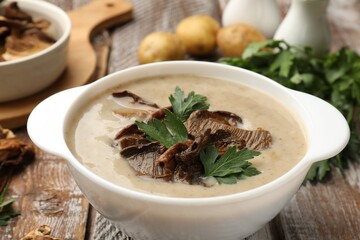 Tasty cream soup with mushrooms and parsley in bowl on color wooden table, closeup