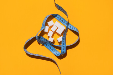 White sugar cubes and measuring tape on yellow background flat lay top view. Concept of sweets consumption and addiction, global health and excess weight issue, sugar-free diet, sports and fitness