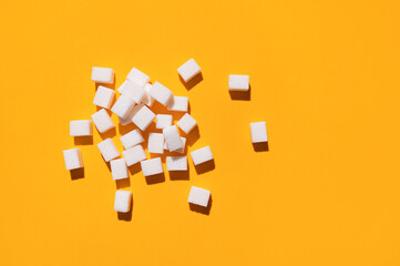 White sugar cubes on yellow background top view flat lay. Scattered sugar cubes. Abstract pattern of food. Concept of sweets consumption and addiction, global issue of health 