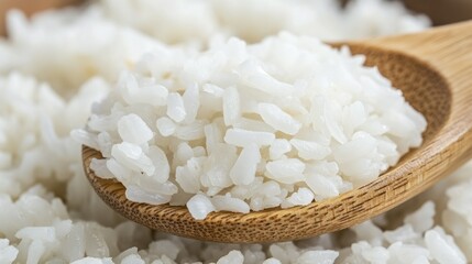 Close-up of cooked white rice on a wooden spoon, nestled within a bowl of more rice