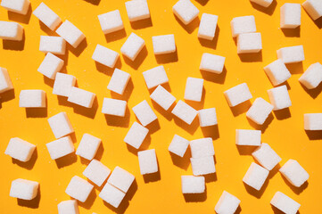 White sugar cubes on yellow background top view flat lay. Scattered sugar cubes. Abstract pattern of food. Concept of sweets consumption and addiction, global issue of health 