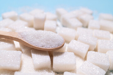 Wooden spoon with sugar and cubes of white refined sugar close-up. Food background, sweetness,...