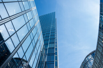 Obraz premium Modern skyscrapers with reflective glass facades rise against a clear blue sky, showcasing architectural design and urban development in a vibrant city environment