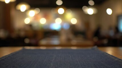 Blurred cafe interior featuring a blue tablecloth on a wooden table in the foreground Bokeh lights and indistinct figures add to the ambiance