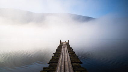 Fototapeta premium Wooden Pier Over Calm Misty Lake at Sunrise with Reflection